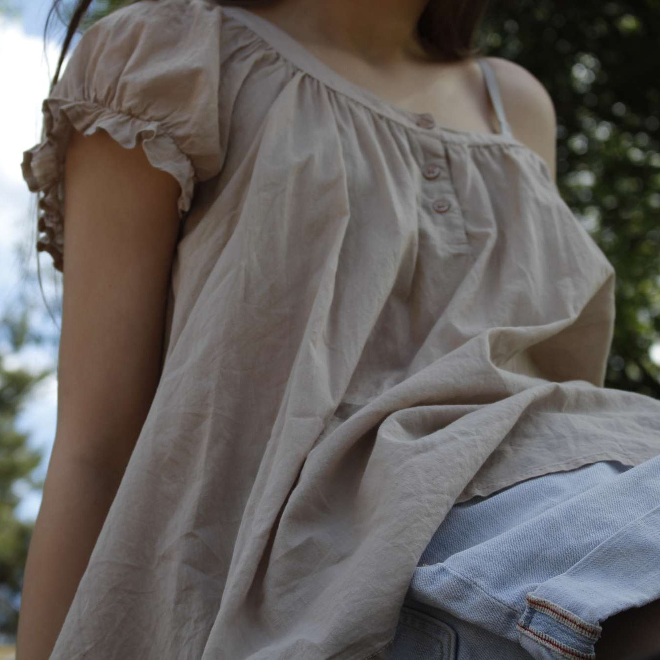 Person wearing a light-colored blouse with ruffled sleeves in an outdoor setting