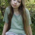 Woman sitting in a forest wearing a light green shirt and gray pants.